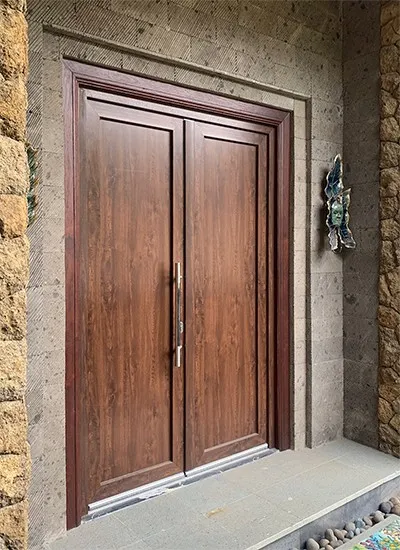 A pair of closed, UPVC double doors in wood decor with a vertical metal handle, set in a stone wall entrance. Smooth stones line the threshold and textured stone surrounds the doorway.